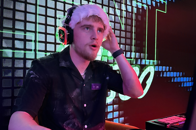 Man wearing a Santa hat and headphones, DJing in a dimly lit room with colorful LED background.