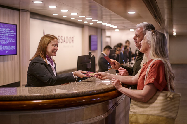 A receptionist hands documents to a smiling couple at the front desk.