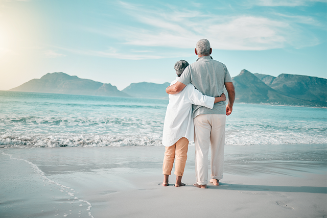 Mature couple hugging on a warm beach looking out to sea