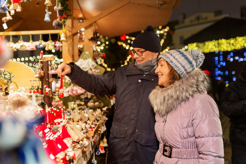 An elderly couple smiles while browsing festive items at a Christmas market stall