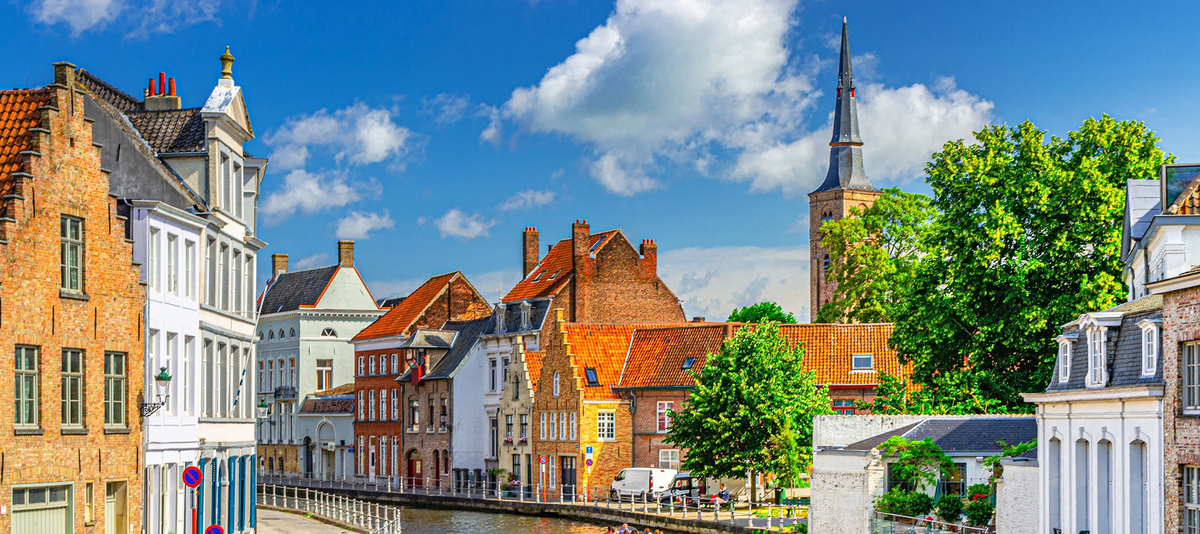 Bruges cityscape, Sint Annarei water canal with tourists boat, medieval houses on embankment in Brugge old town quarter, Bruges city historical center, Saint Anna catholic Church tower spire, Belgium