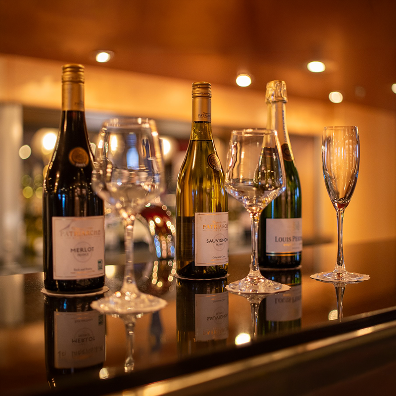 Three wine bottles and four empty glasses on a bar counter